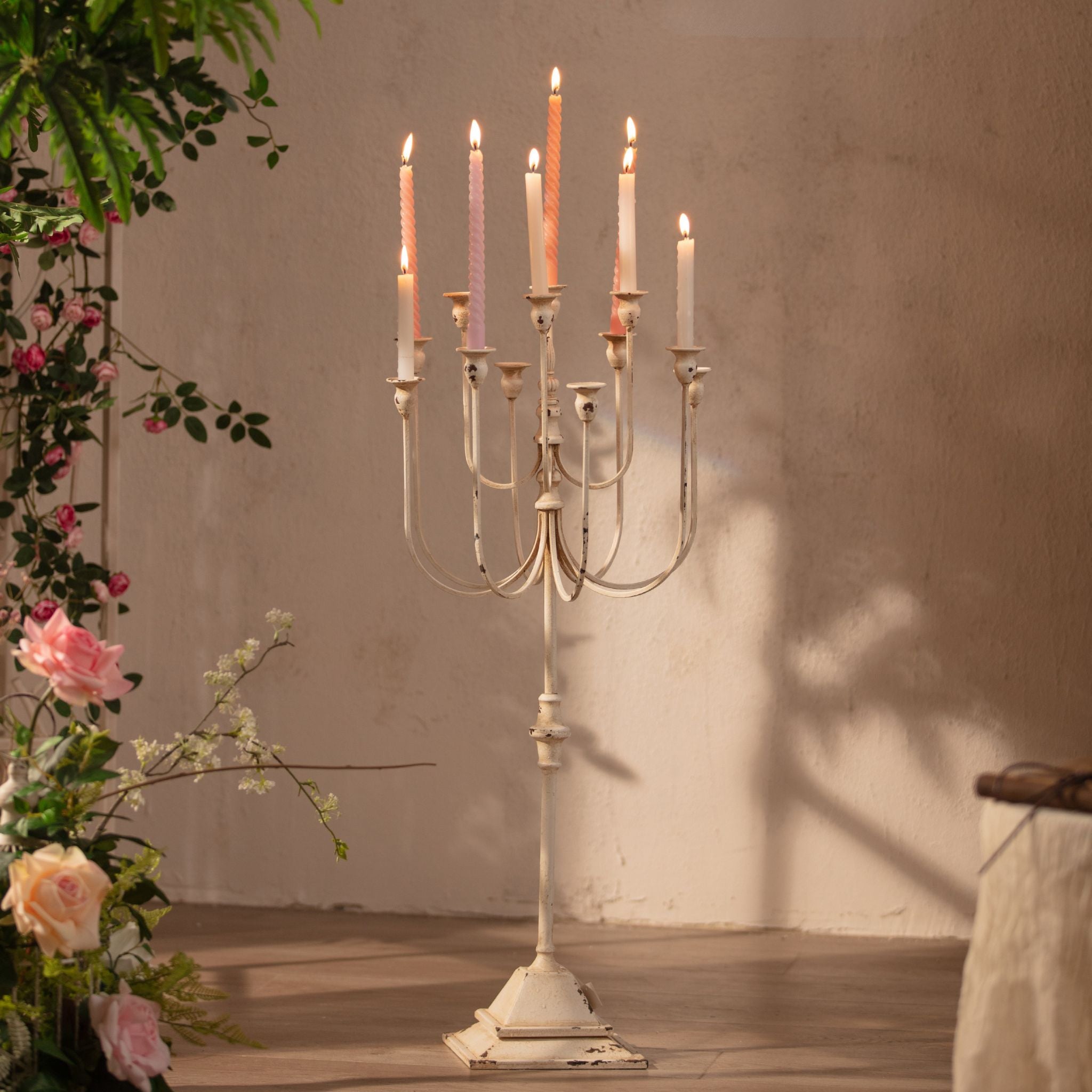 Laetitia tall distressed cream floor candelabra lit with taper candles against a plaster wall. Hero.