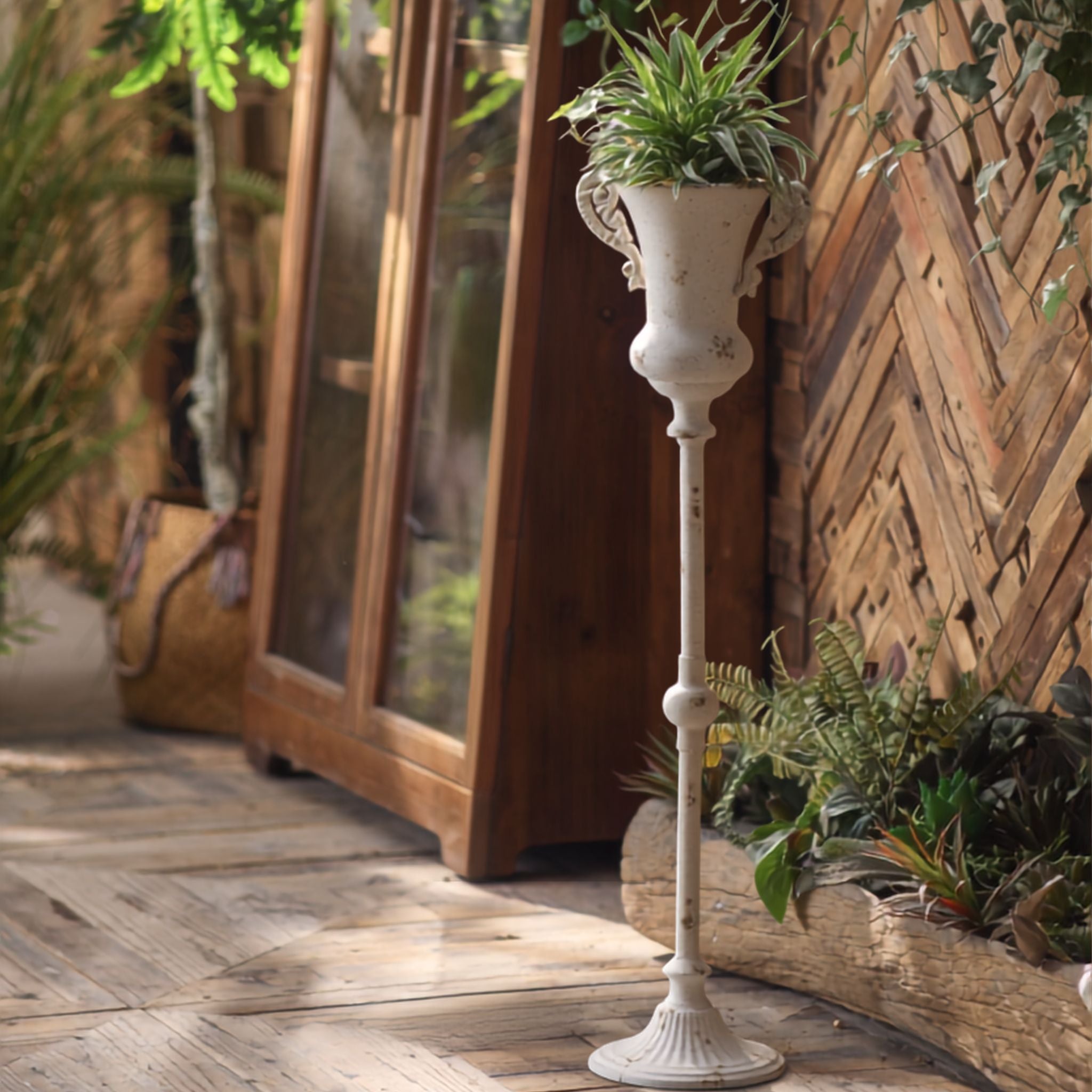Thierry tall pedestal urn in distressed antique white, planted with greenery, on a timber verandah. Hero.