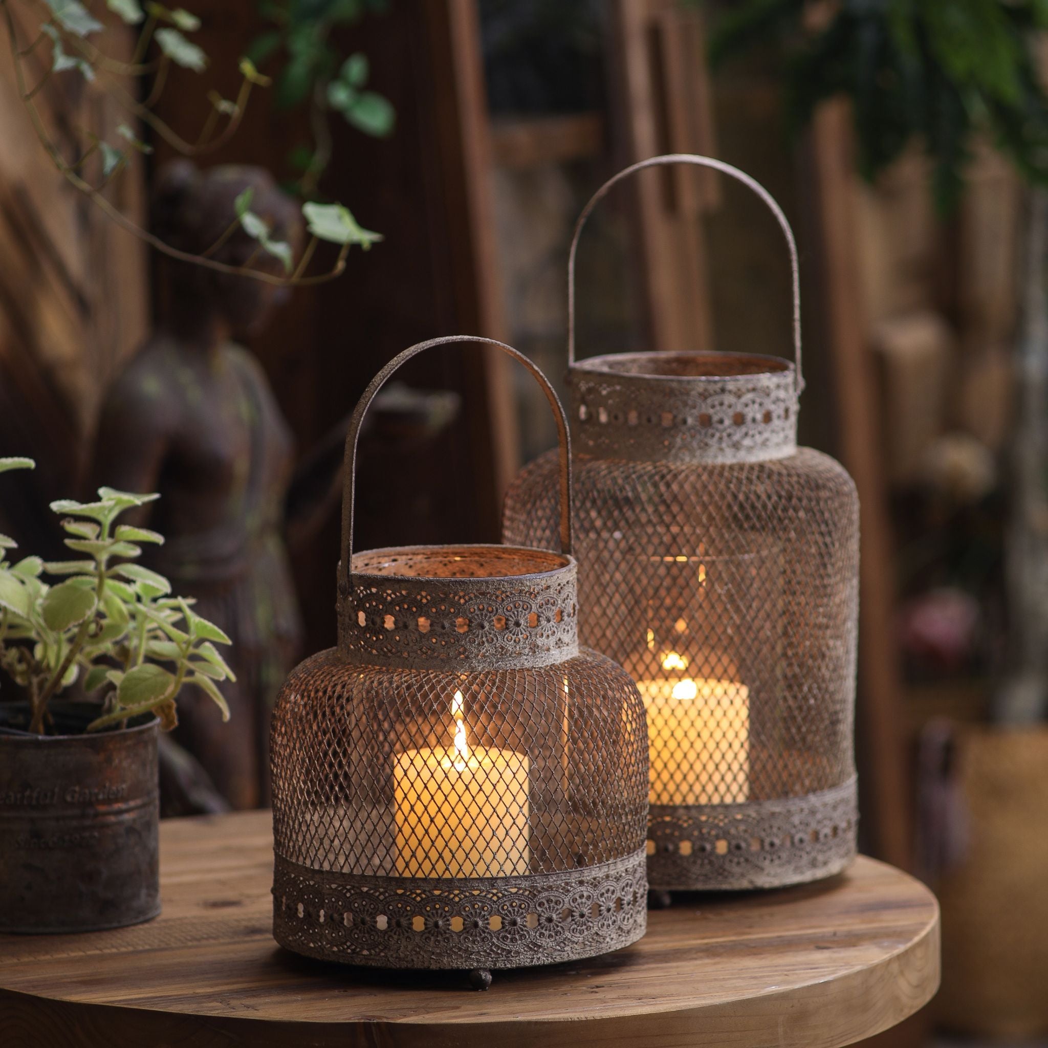 Two mesh candle lanterns in two sizes, both lit on a table