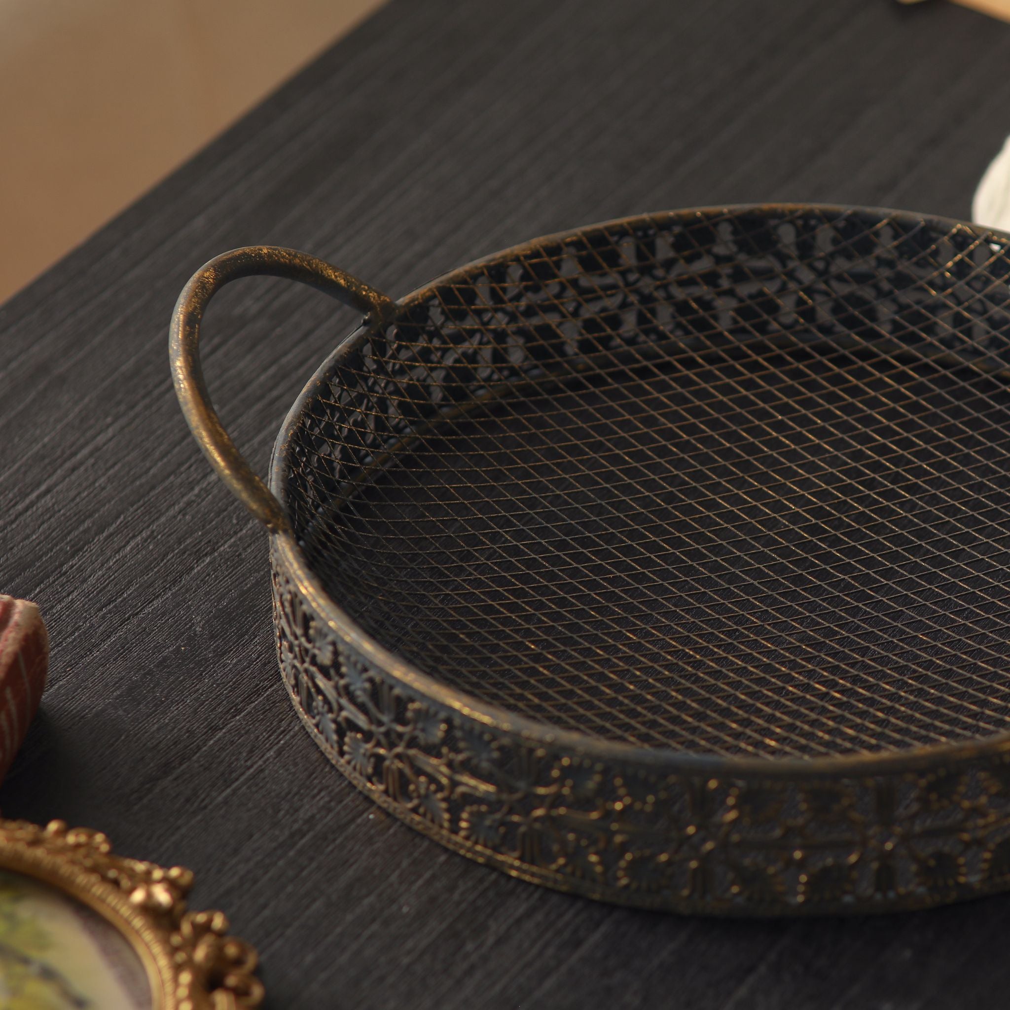 Close detail of the Valerie tray, fine wire mesh base and stamped filigree side in antique gold over dark metal.
