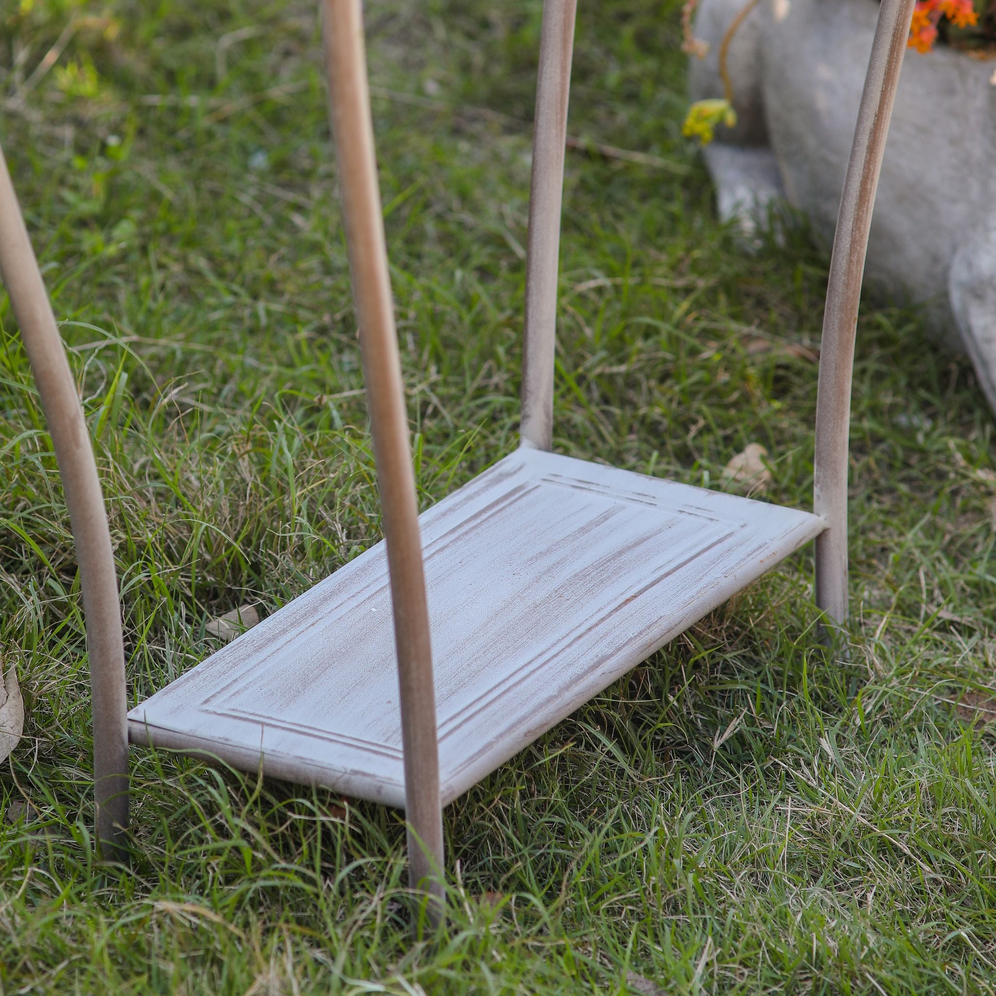 Close-up of the lower shelf and curved legs of the Yolande plant stand on grass.